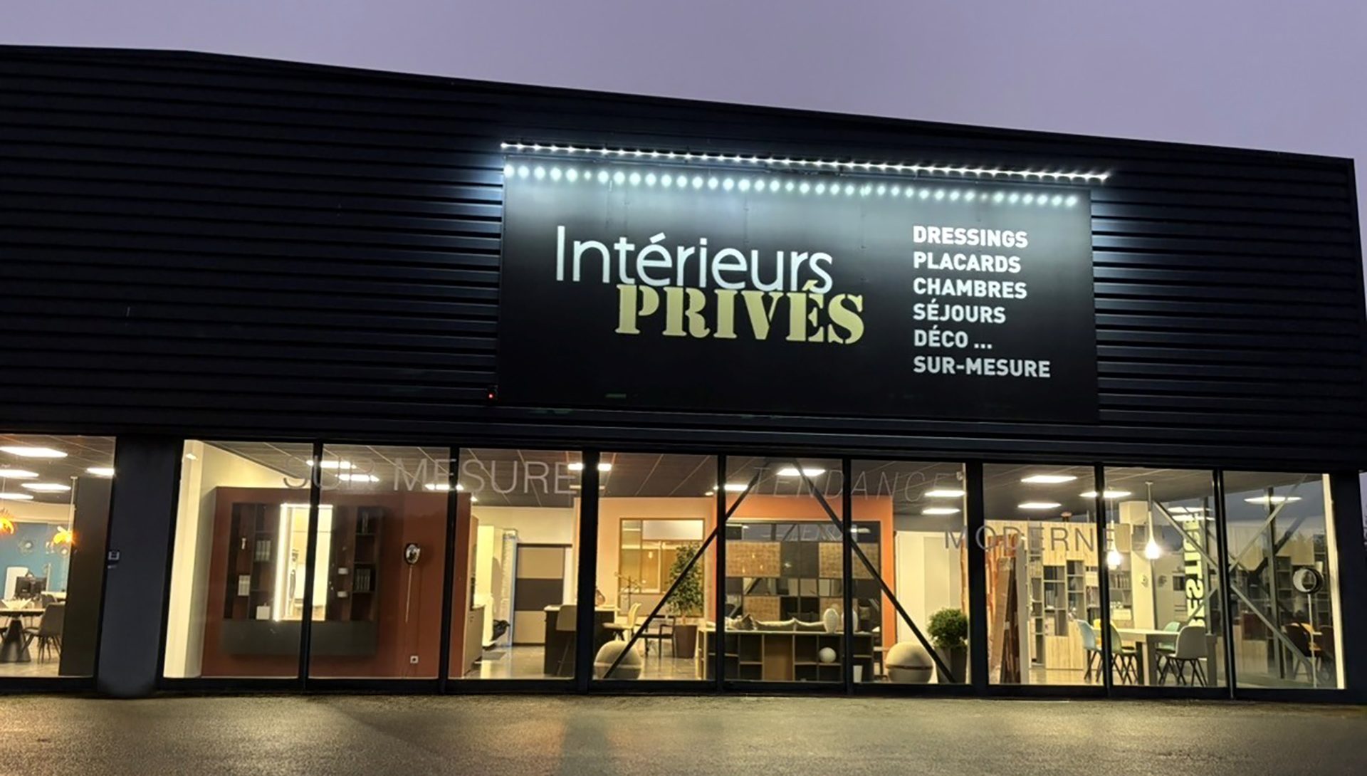 Façade du magasin Intérieurs Privés à Chartres, spécialisé dans les dressings, placards, chambres et aménagements intérieurs sur mesure. Le showroom présente en vitrine plusieurs espaces d’exposition dédiés aux rangements personnalisés, aux solutions déco et aux agencements de pièces à vivre. Photo prise en soirée, mettant en valeur la signalétique lumineuse du magasin.