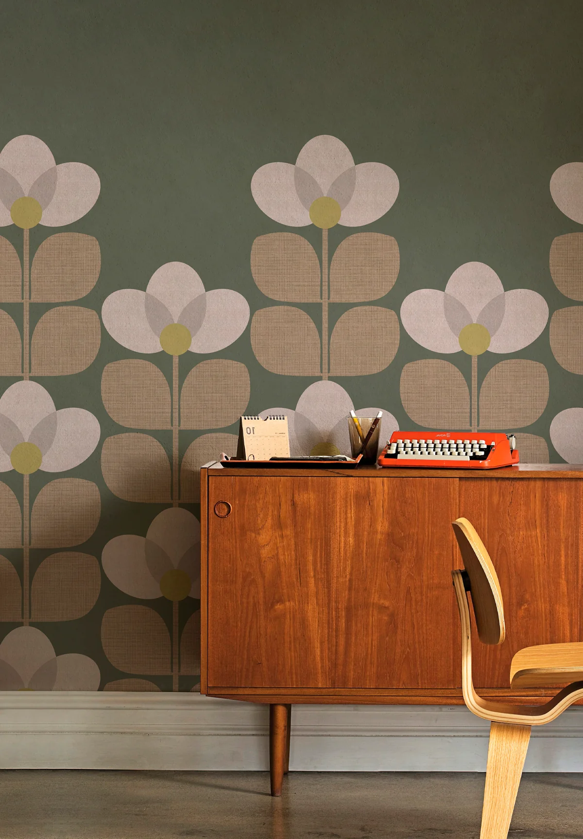 Papier peint Flower sur mesure signé Isidore Leroy, aux motifs floraux géométriques beige et vert olive, associé à un meuble vintage en bois. Un design emblématique du style POP Revival, idéal pour habiller un salon ou un bureau avec caractère.