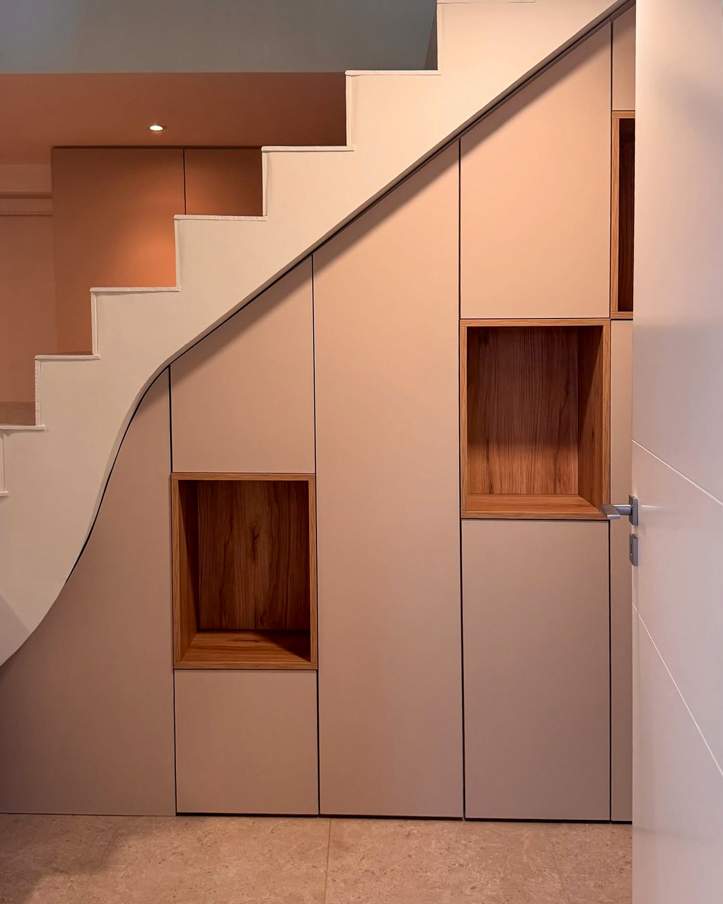 Adoptez un rangement astucieux sous votre escalier grâce à ce placard sur mesure au style minimaliste. Les niches en bois naturel intégrées apportent du caractère et permettent d’exposer des objets déco tout en maximisant la fonctionnalité de l’espace.