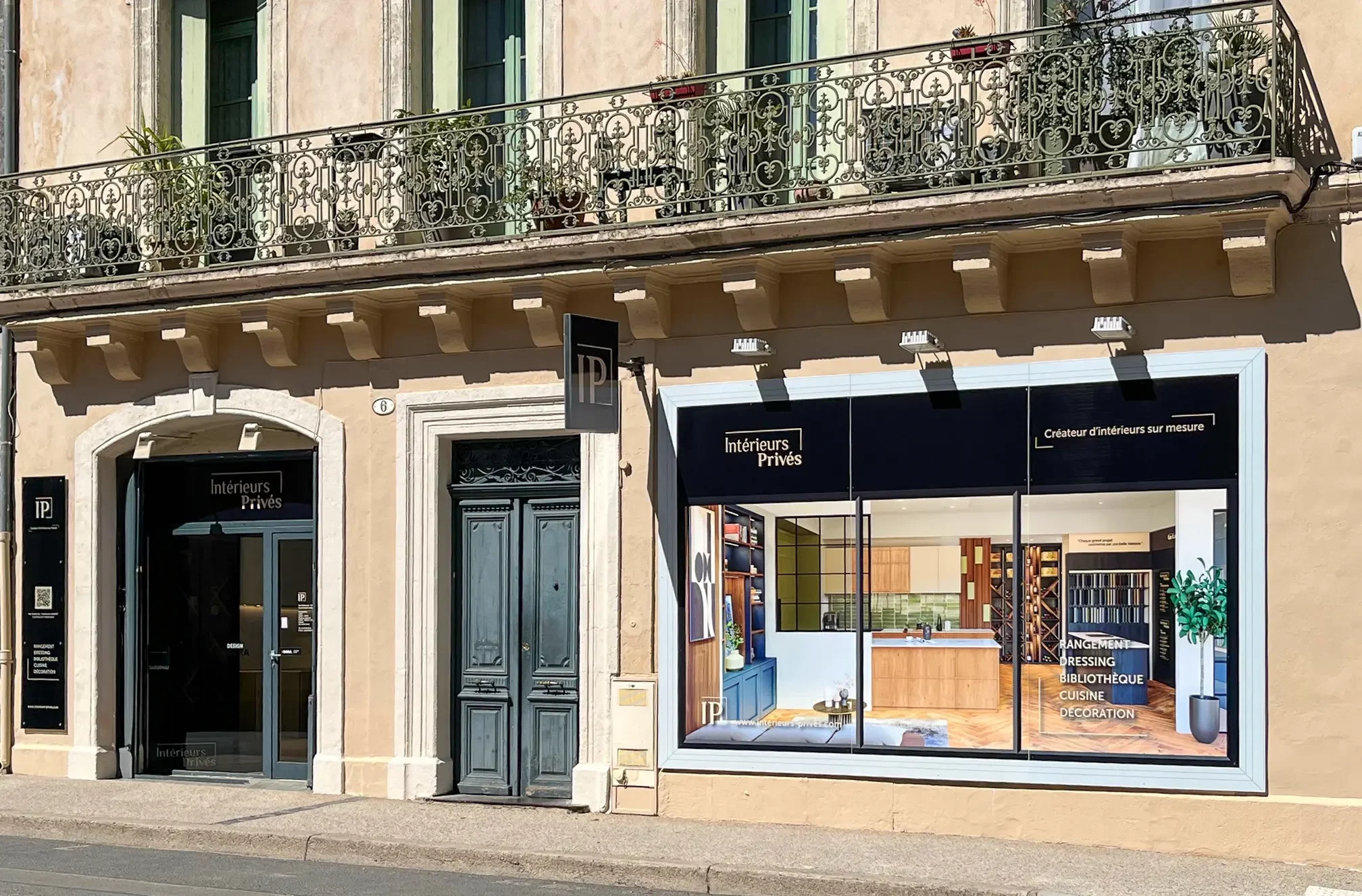 Façade du showroom Interieurs Privés à Pézenas, concepteur de cuisines et rangements sur mesure. On y voit la vitrine moderne avec des visuels d'aménagements intérieurs et l'entrée du magasin dans un bâtiment historique.