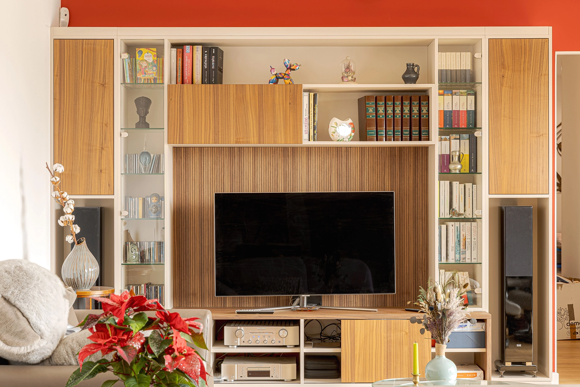 Aménagement TV intégrant rangements bas techniques, niches ouvertes, modules fermés en décor bois et étagères vitrées pour organiser livres, appareils multimédias et objets décoratifs.