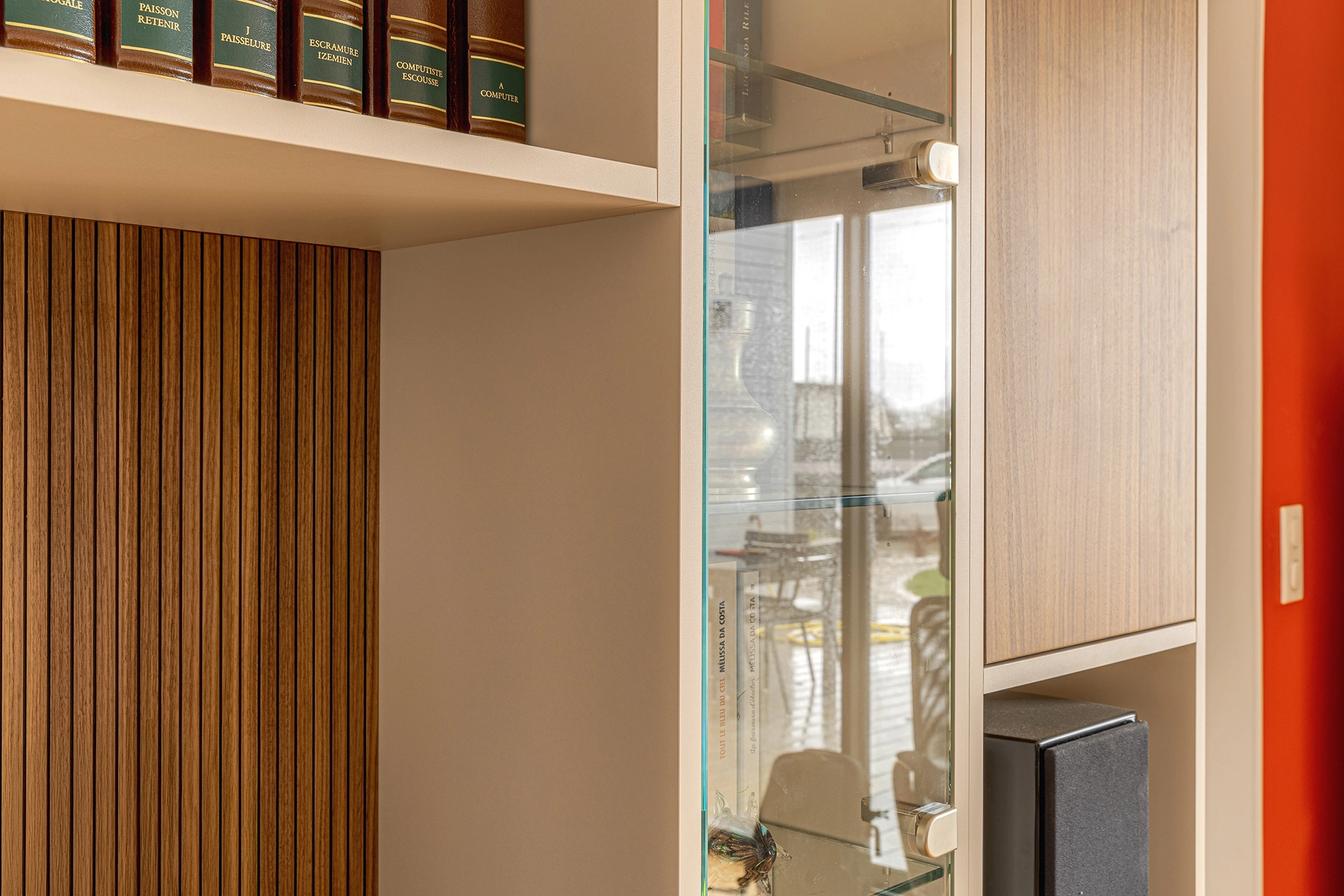 Détail d’angle du meuble TV sur mesure montrant la jonction entre la vitrine en verre, la structure beige et le décor bois, soulignant la qualité des matériaux et l’intégration dans le salon. Intérieurs Privés Vannes