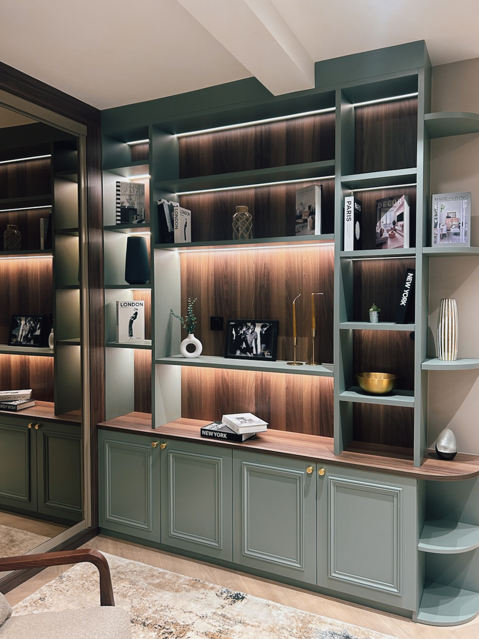 Bibliothèque sur mesure exposée chez Intérieurs Privés Paris 6, associant façades vert profond, niches rétroéclairées et fonds bois. Un aménagement pensé pour structurer l’espace et mettre en valeur objets et ouvrages.