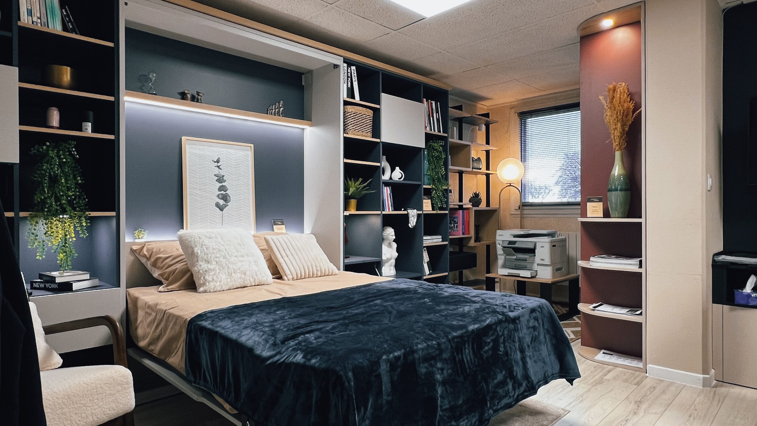 Aménagement de chambre sur mesure exposé au showroom Intérieurs Privés de Saint-Germain-en-Laye, intégrant un lit escamotable, des bibliothèques et des rangements fonctionnels. Une solution idéale pour optimiser l’espace sans compromis esthétique.