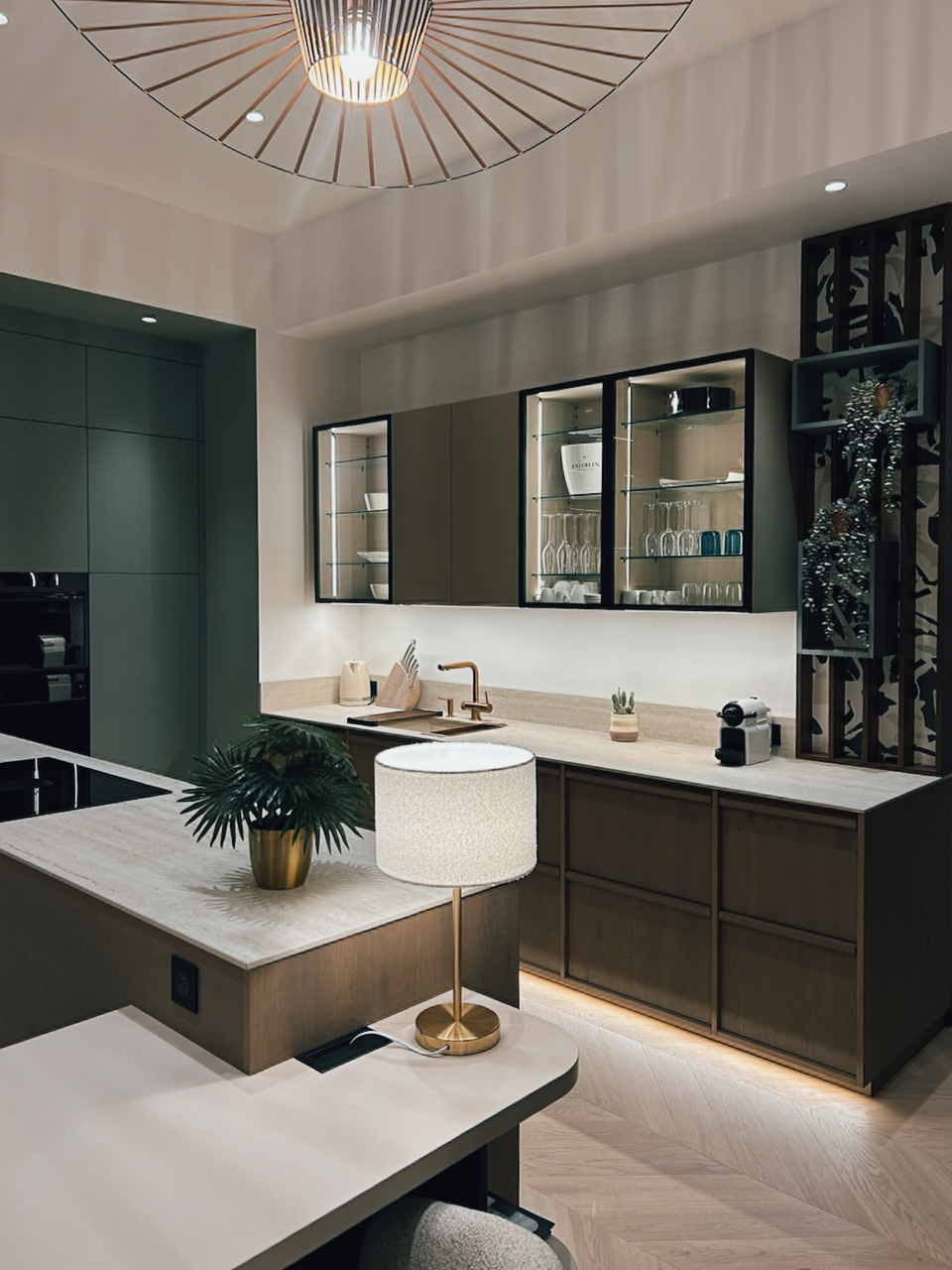 Cuisine sur mesure présentée au showroom Intérieurs Privés Paris 6, avec vitrines éclairées, plan de travail clair, îlot central et façades vert profond. Un aménagement qui met en valeur les volumes et les usages du quotidien.
