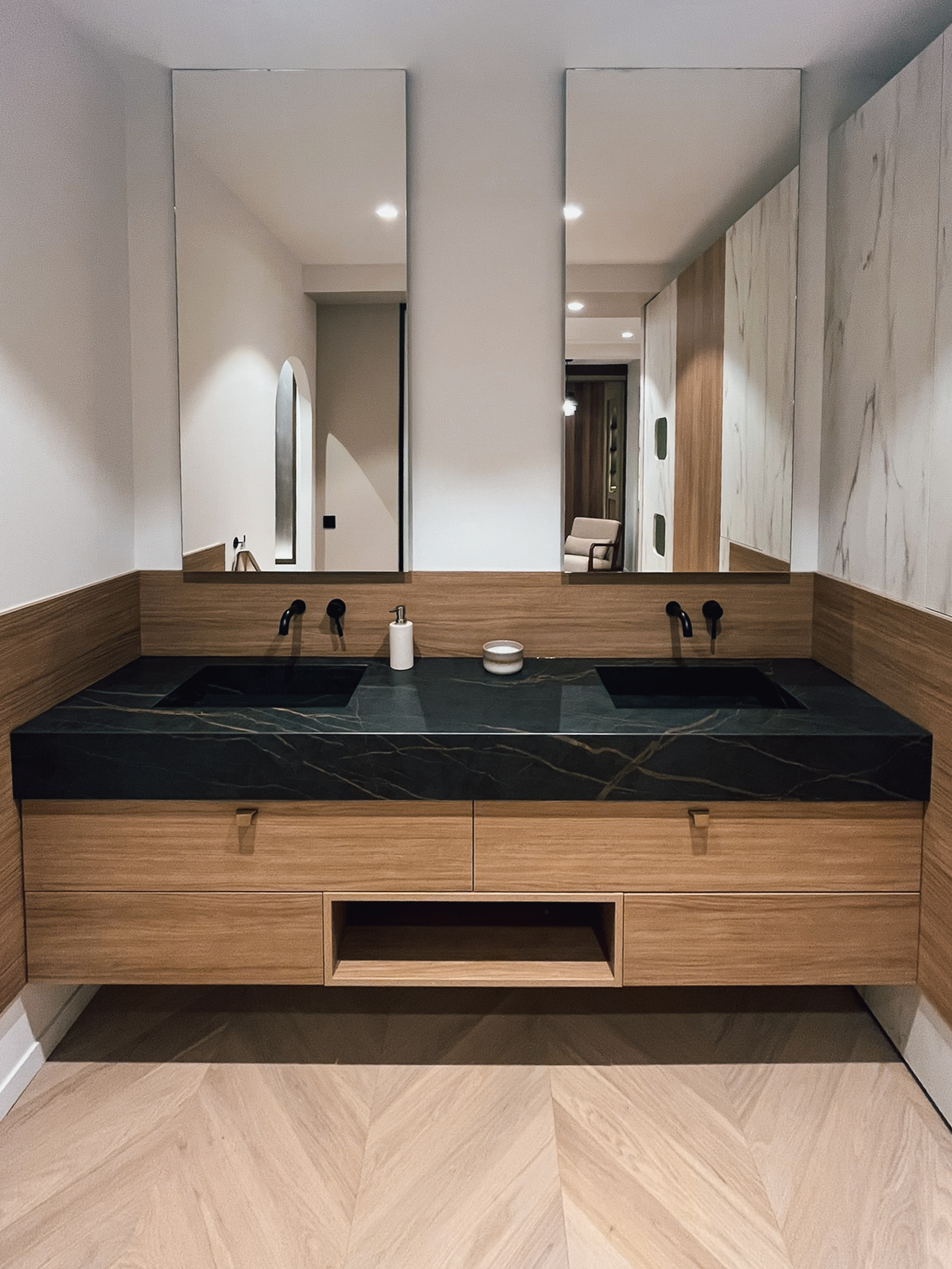 Salle de bain sur mesure présentée au showroom Intérieurs Privés Paris 6 : meuble en bois, double vasque intégrée, plan minéral sombre et robinetterie murale. Une composition équilibrée entre fonctionnalité et qualité des matériaux.