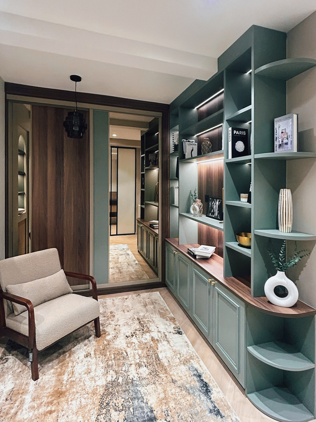 Vue d’ensemble d’un espace salon exposé chez Intérieurs Privés Paris 6, combinant bibliothèque sur mesure, rangements bas, éclairage intégré et finitions bois et vert mat. Une démonstration du savoir-faire en agencement intérieur sur mesure.