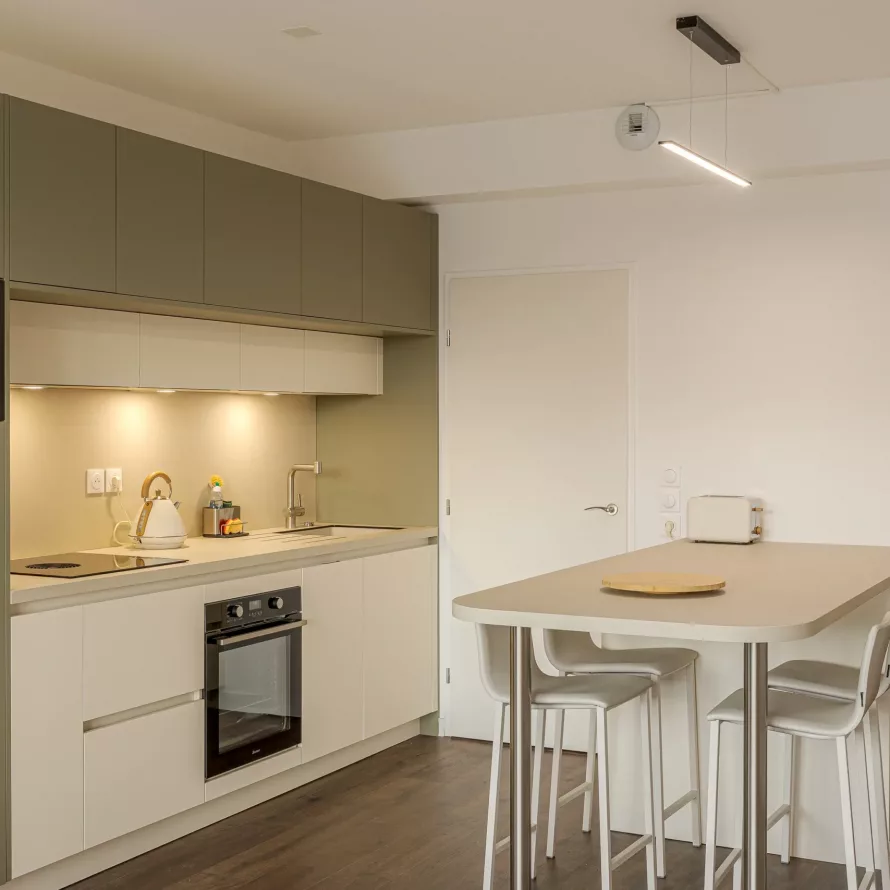 Cuisine sur mesure ouverte avec table snack, façades vert sauge et blanches, et circulation dégagée