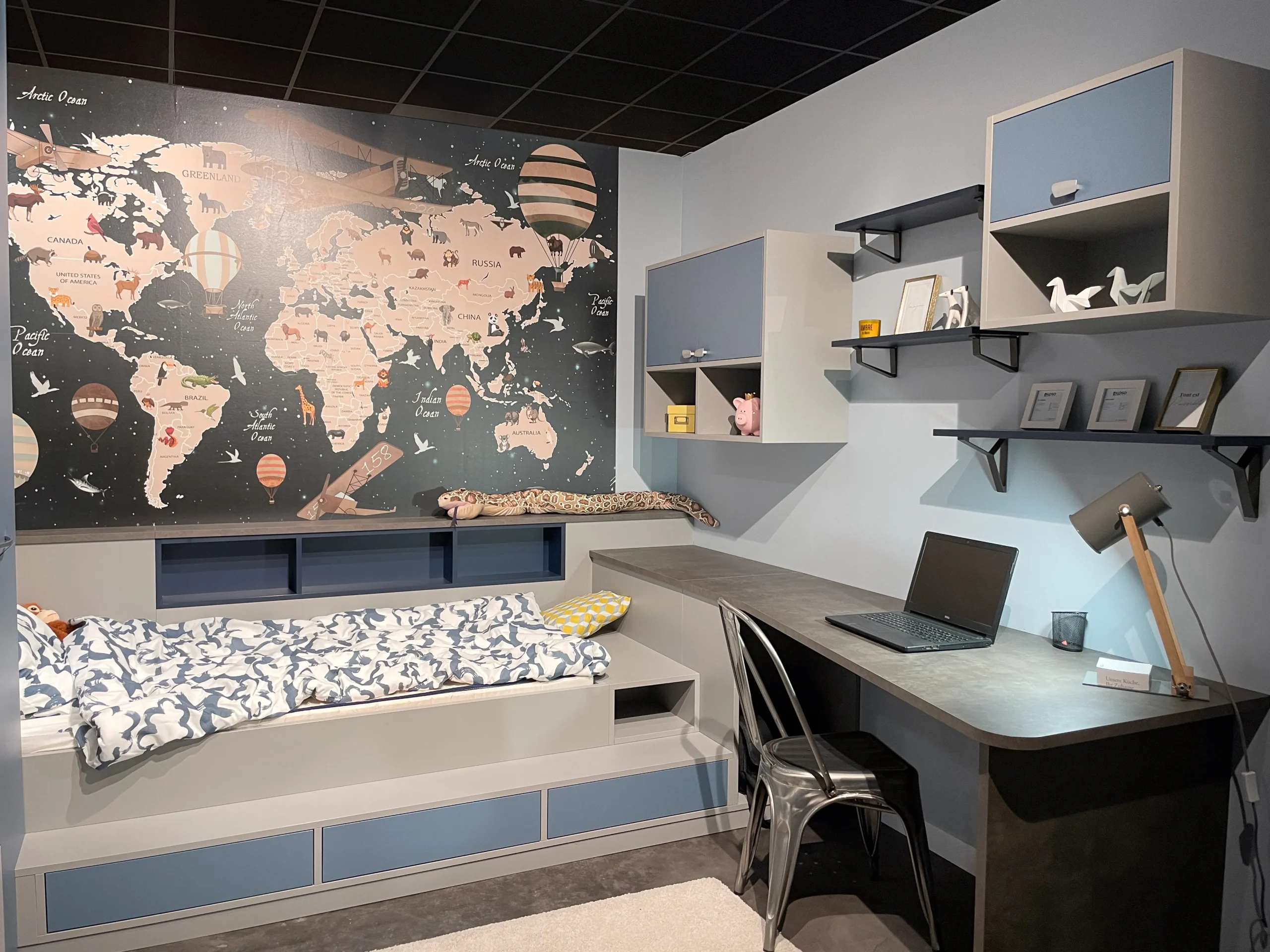Chambre enfant sur-mesure avec lit banquette, bureau intégré, rangements muraux et grand papier peint carte du monde.