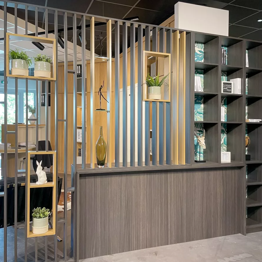 Grand claustra bibliothèque en bois foncé et bois clair, avec niches végétalisées, étagères ouvertes et séparation ajourée entre deux espaces.