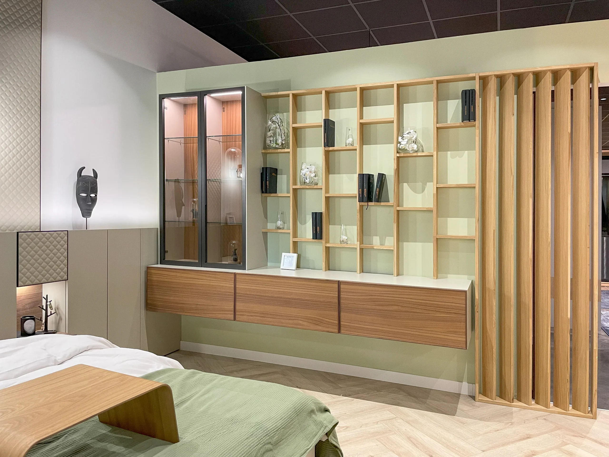 Aménagement mural sur-mesure avec claustra en bois, bibliothèque ouverte, vitrine éclairée et rangements bas suspendus.