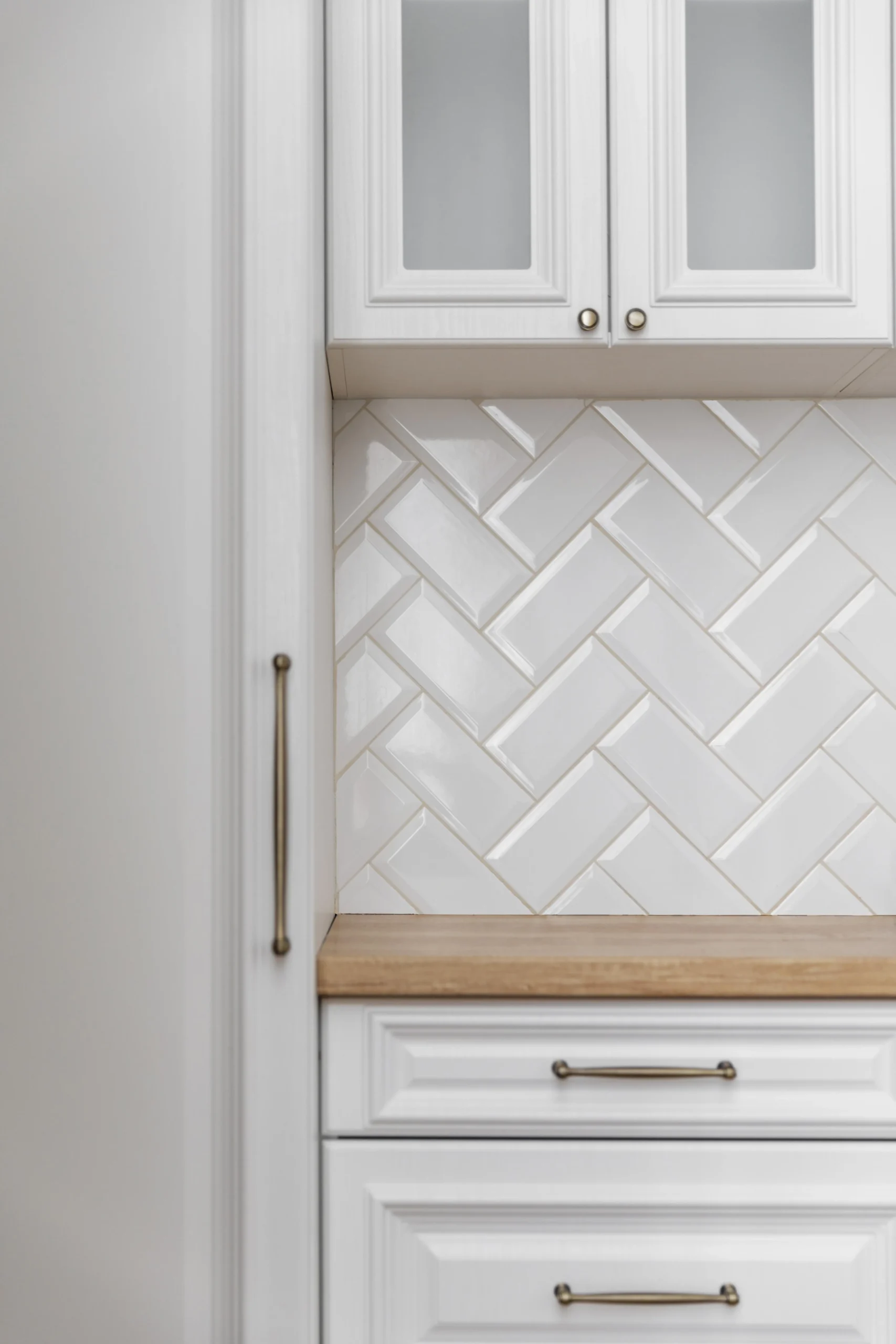 Cuisine blanche classique avec façades moulurées, poignées finition laiton, plan de travail bois clair et crédence en carreaux métro.