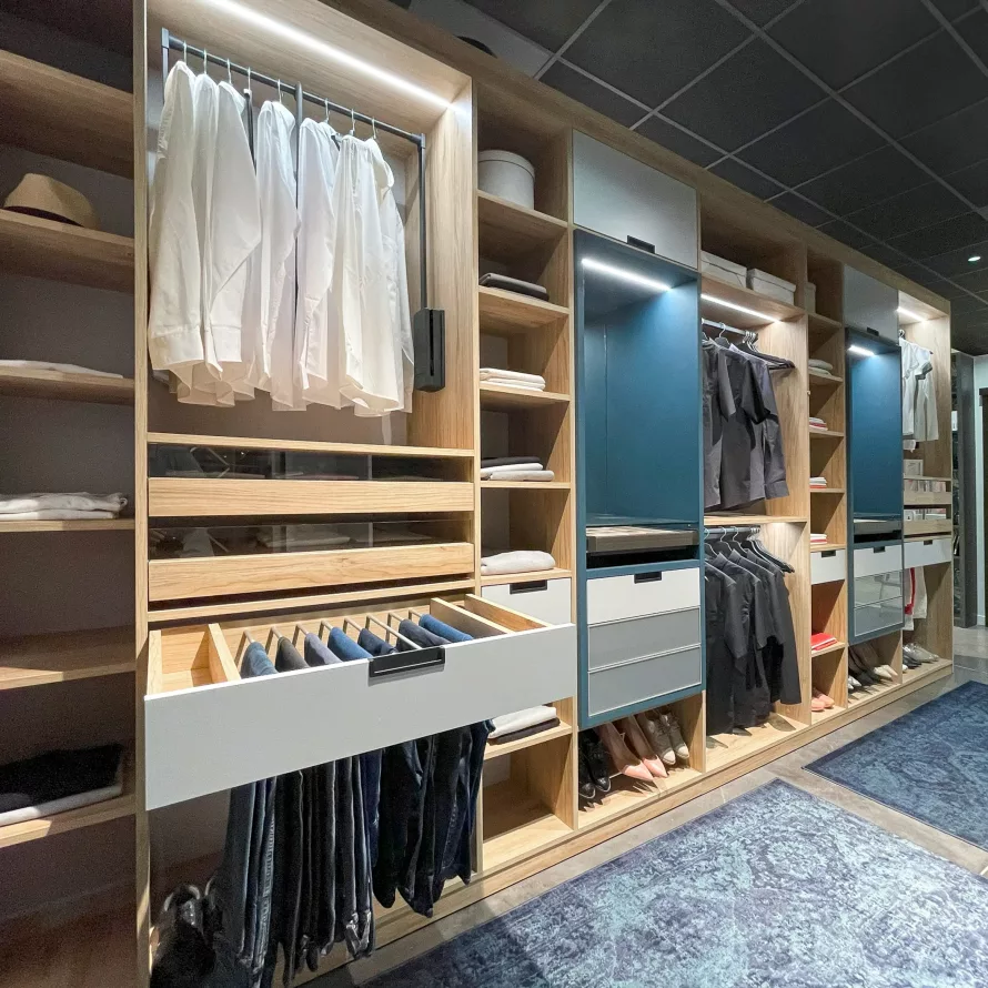 Dressing sur-mesure avec penderies éclairées, chemises suspendues, tiroirs vitrés et étagères ouvertes en bois clair.