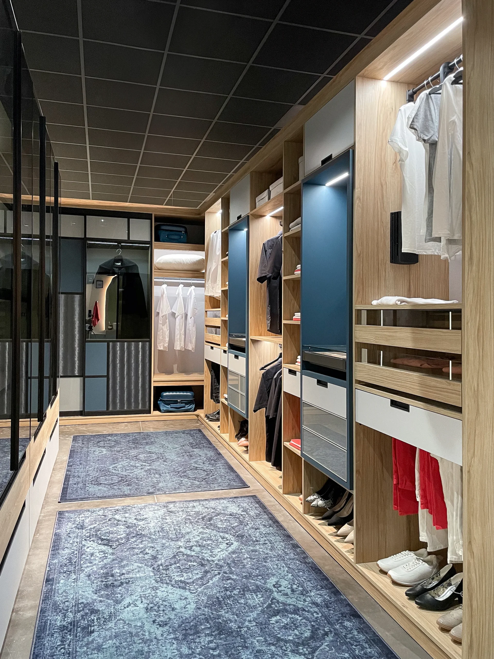 Dressing linéaire sur-mesure avec penderies ouvertes, tiroirs intégrés, rangements à chaussures et portes vitrées noires en fond.