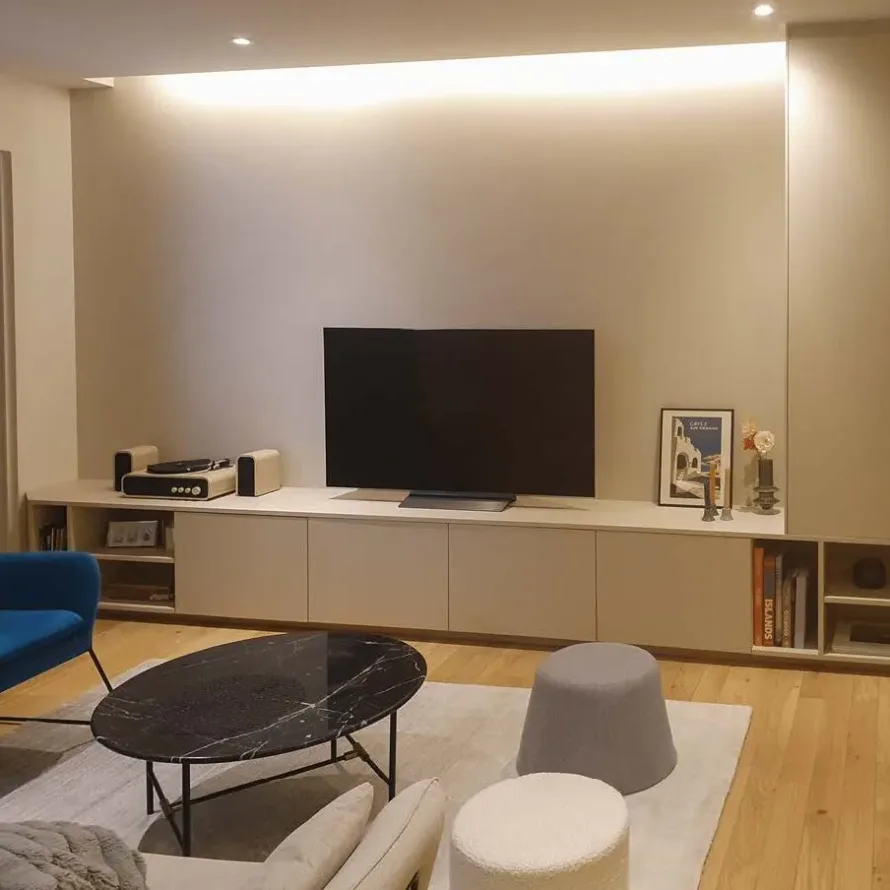 Salon avec meuble TV sur-mesure beige, rangements bas, niches ouvertes et éclairage indirect chaleureux.