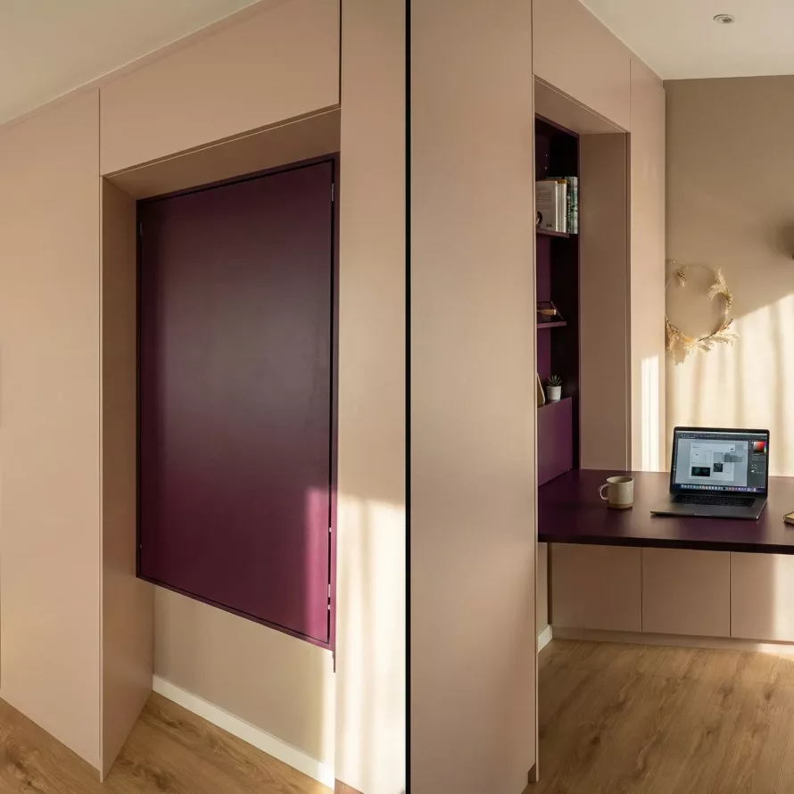Aménagement sur-mesure avec bureau escamotable, rangements intégrés, façade rose poudré et niche décorative.