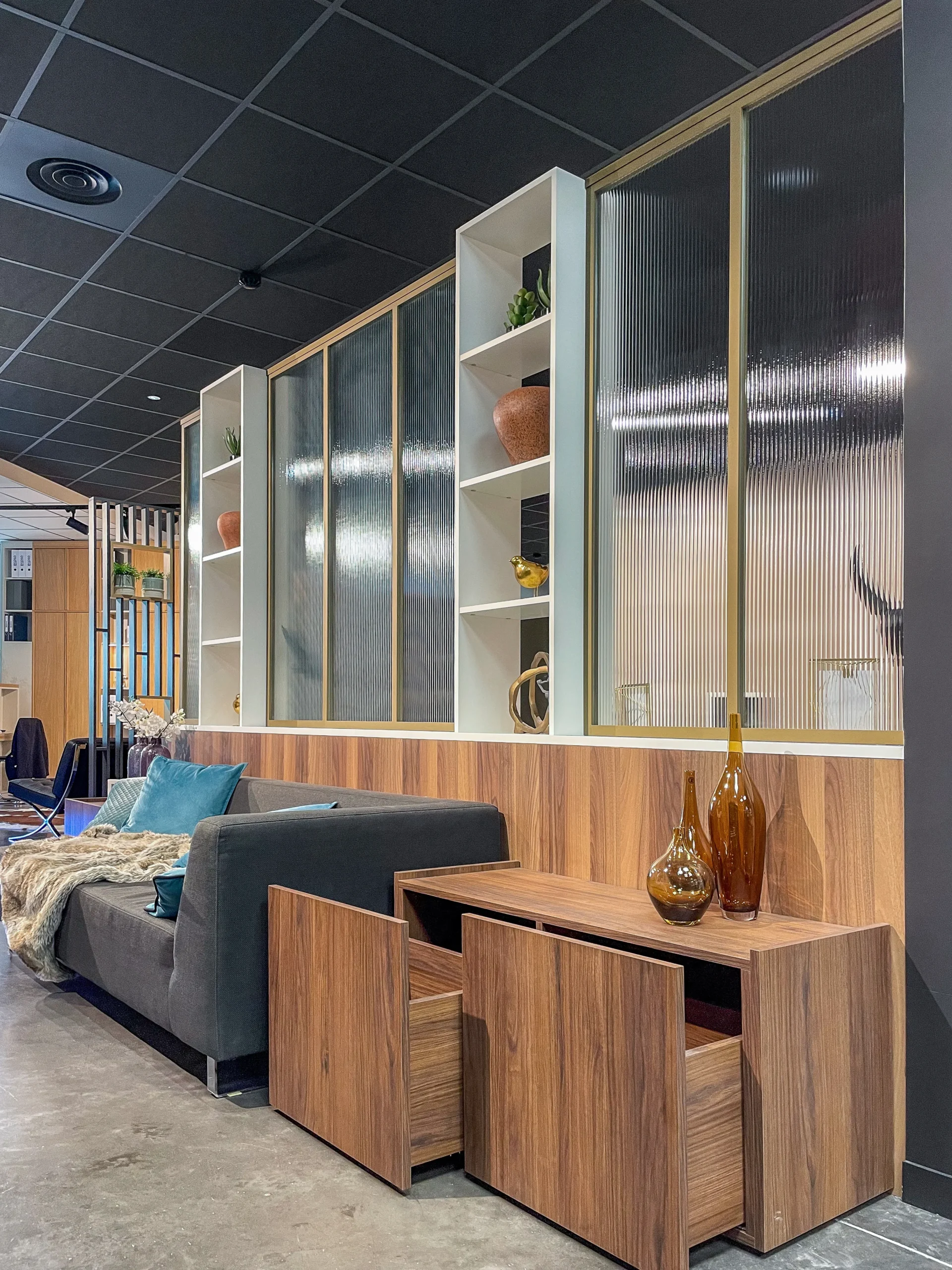 Habillage mural en bois avec façades vitrées, niches ouvertes et meubles bas assortis autour d’un espace canapé.