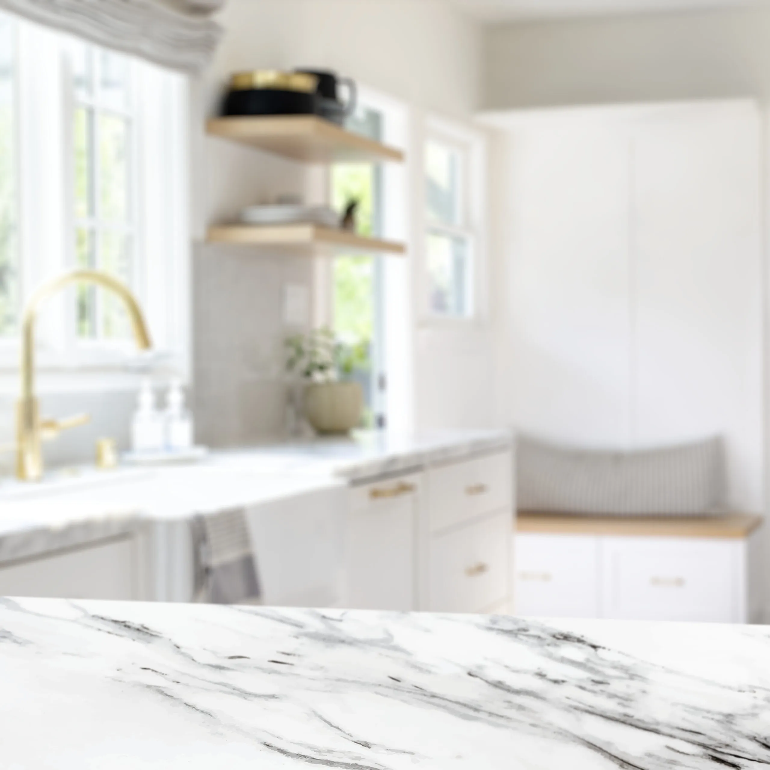 Gros plan sur un plan de travail effet marbre blanc dans une cuisine claire avec robinet doré, étagères murales et banquette intégrée.