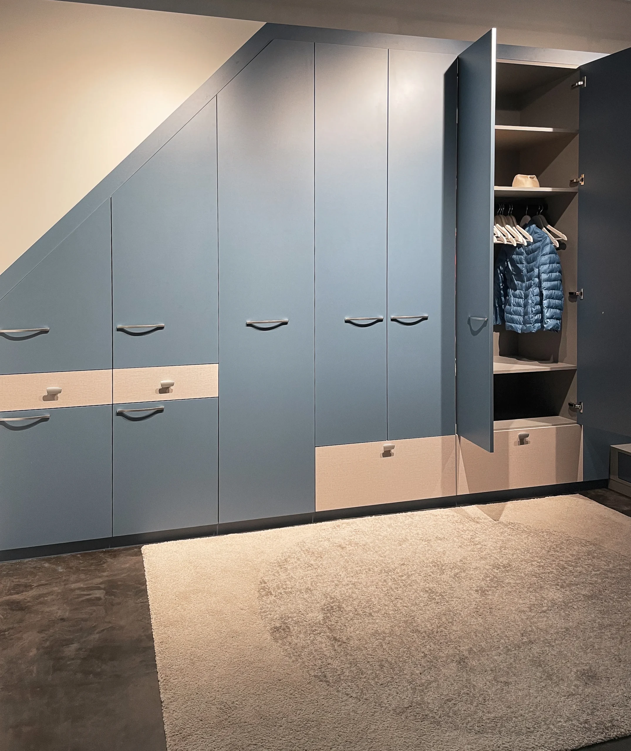 Placard sous-pente bleu ouvert avec penderie, étagères intérieures et tiroirs bas pour organiser vêtements et chaussures.