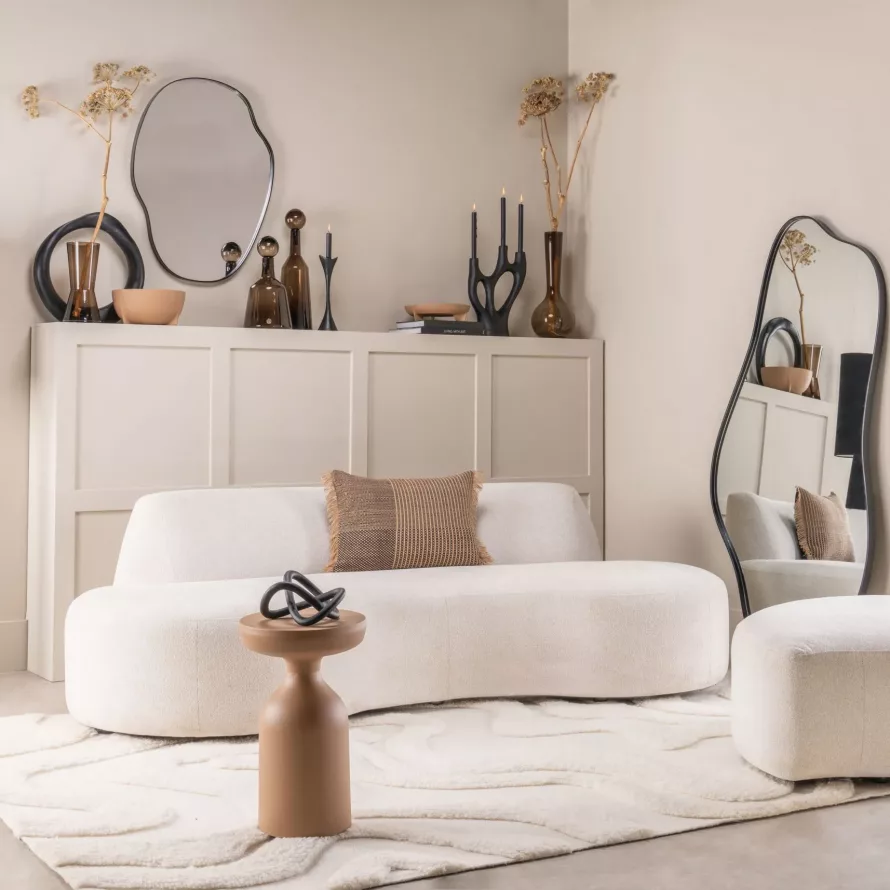 Salon lumineux avec canapé blanc, miroir organique, objets décoratifs et ambiance douce aux tons naturels.