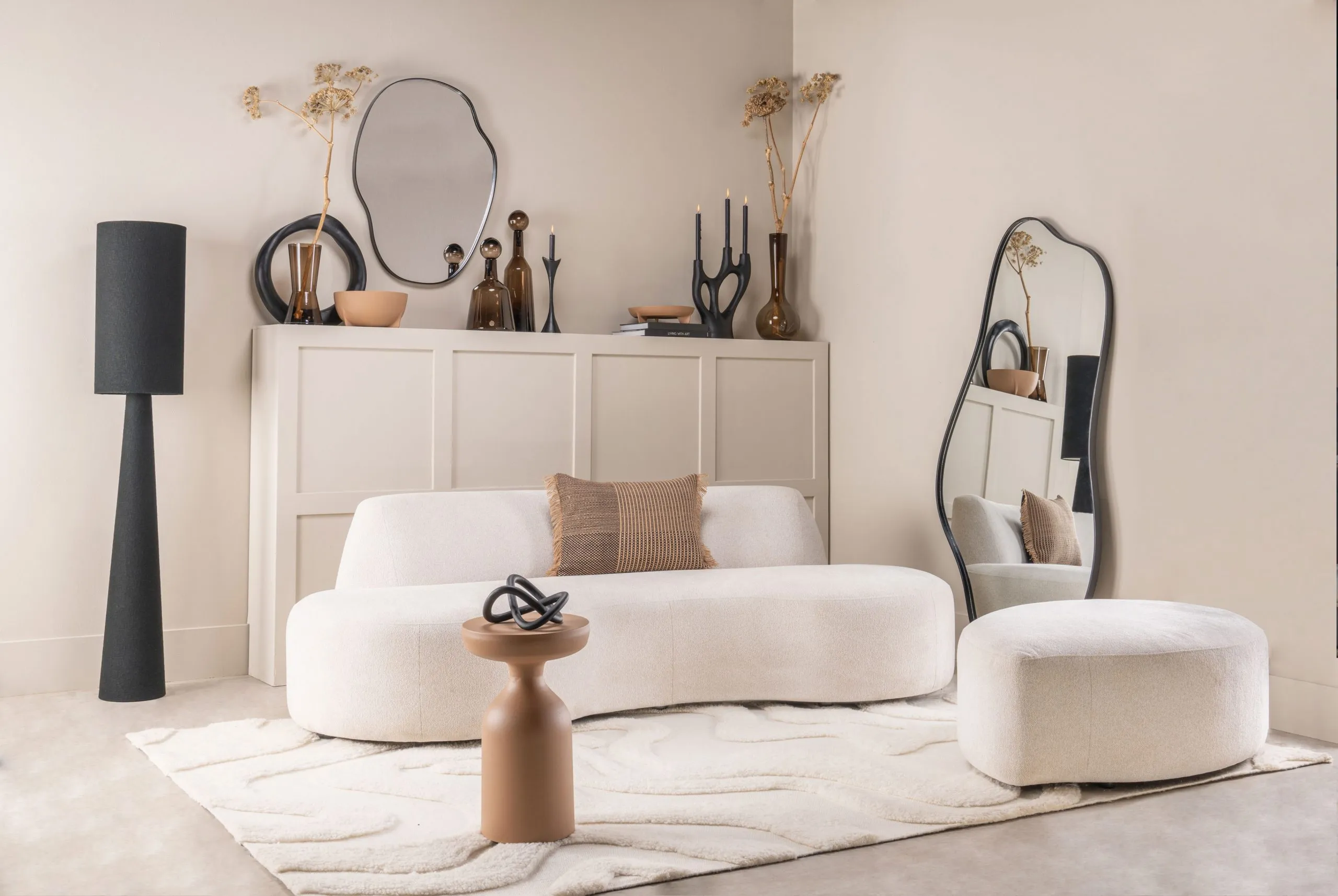 Salon lumineux avec canapé blanc, miroir organique, objets décoratifs et ambiance douce aux tons naturels.