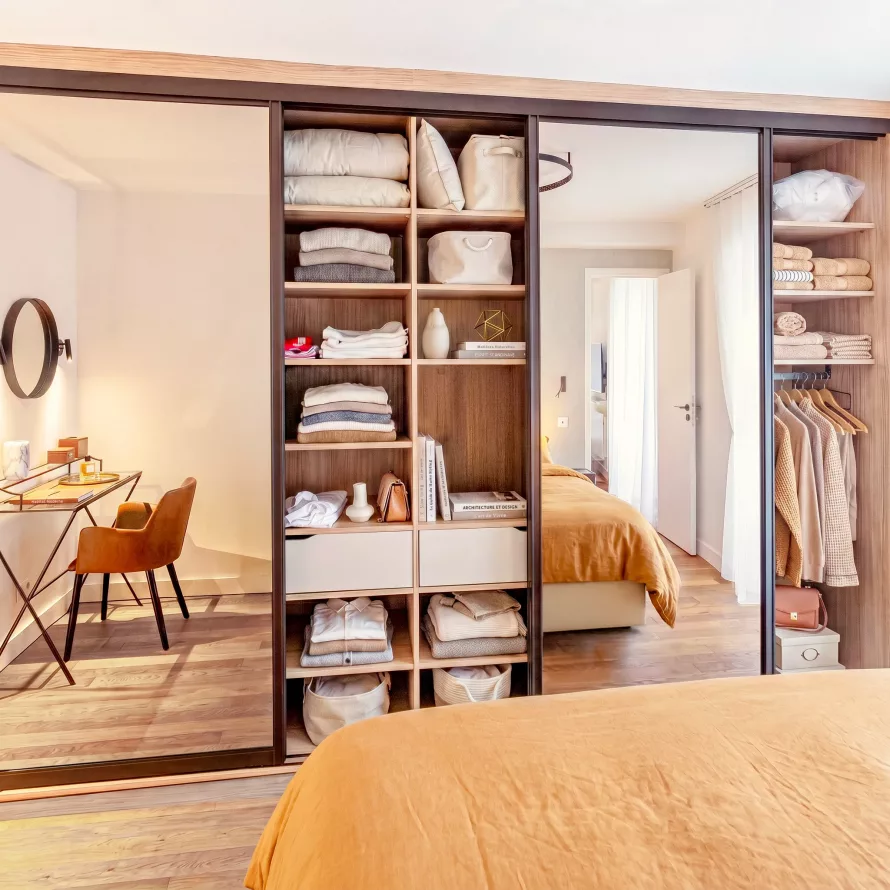 Dressing sur-mesure avec portes coulissantes miroir, étagères ouvertes, penderie et espace bureau intégré dans une suite parentale lumineuse.