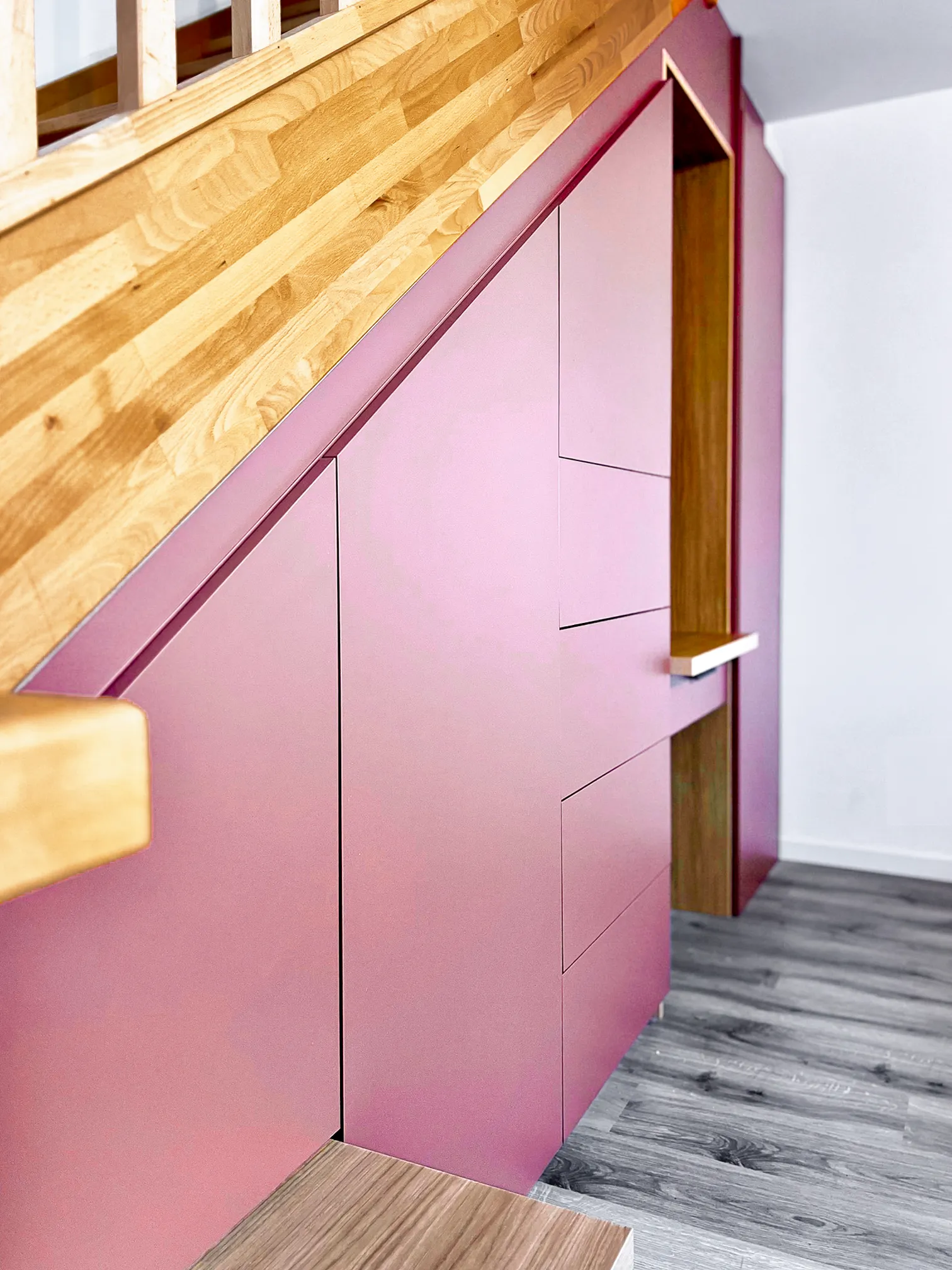 Aménagement sous escalier sur-mesure avec façades rose poudré, niches bois et garde-corps en bois naturel.