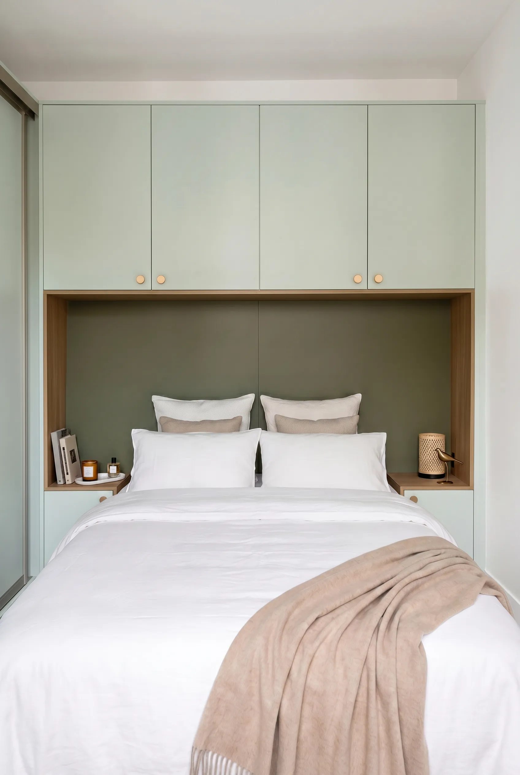 Chambre avec aménagement sur-mesure vert sauge autour du lit, rangements hauts, niches en bois, tables de chevet intégrées et portes de placard coulissantes.