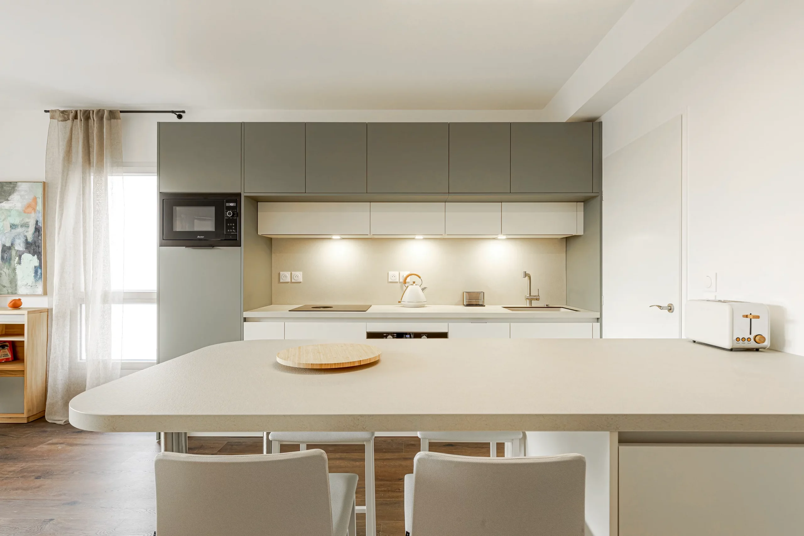 Cuisine sur mesure avec coin repas attenant, rangements muraux vert sauge et façades blanches