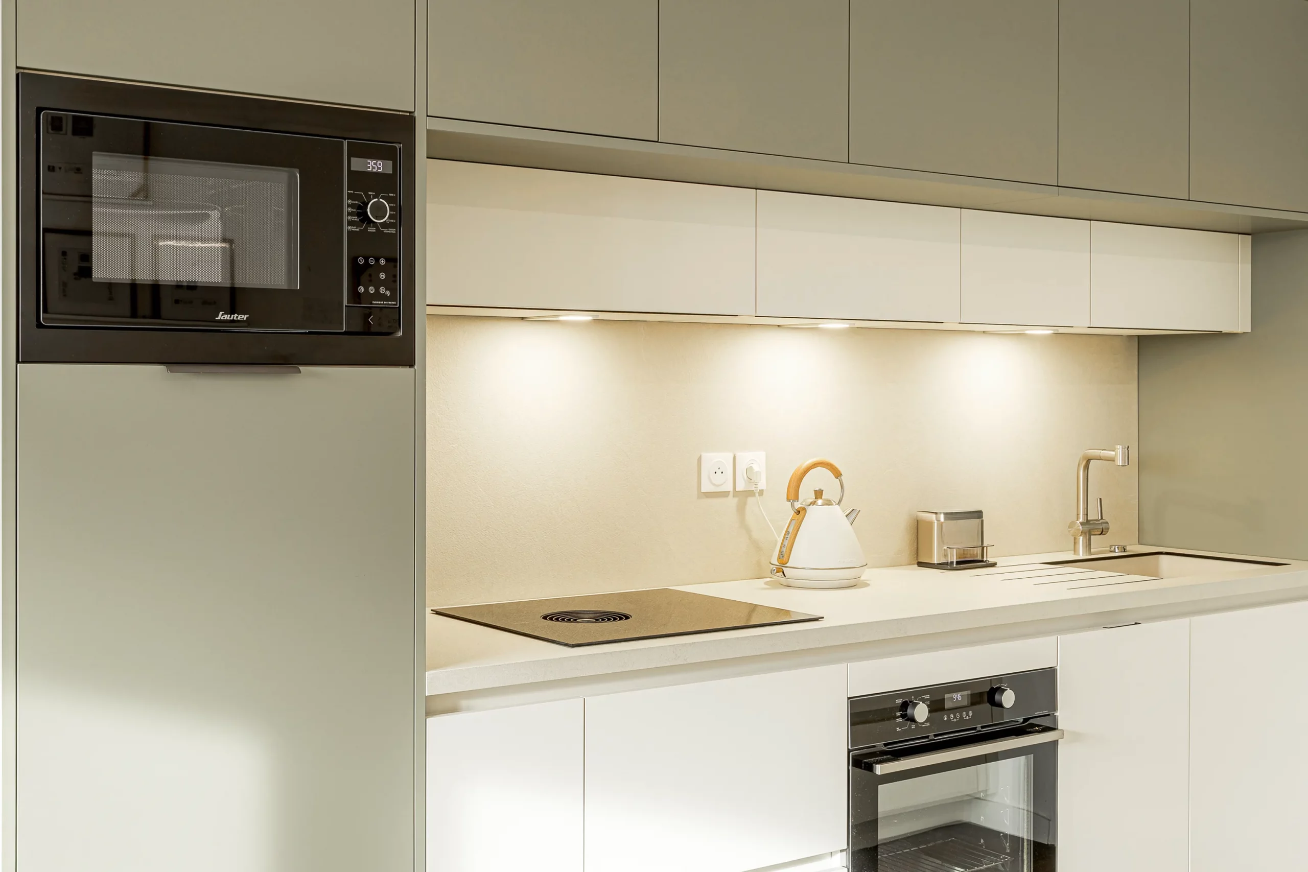 Cuisine compacte sur mesure avec colonne intégrant le micro-ondes, rangements hauts vert sauge et plan de travail clair