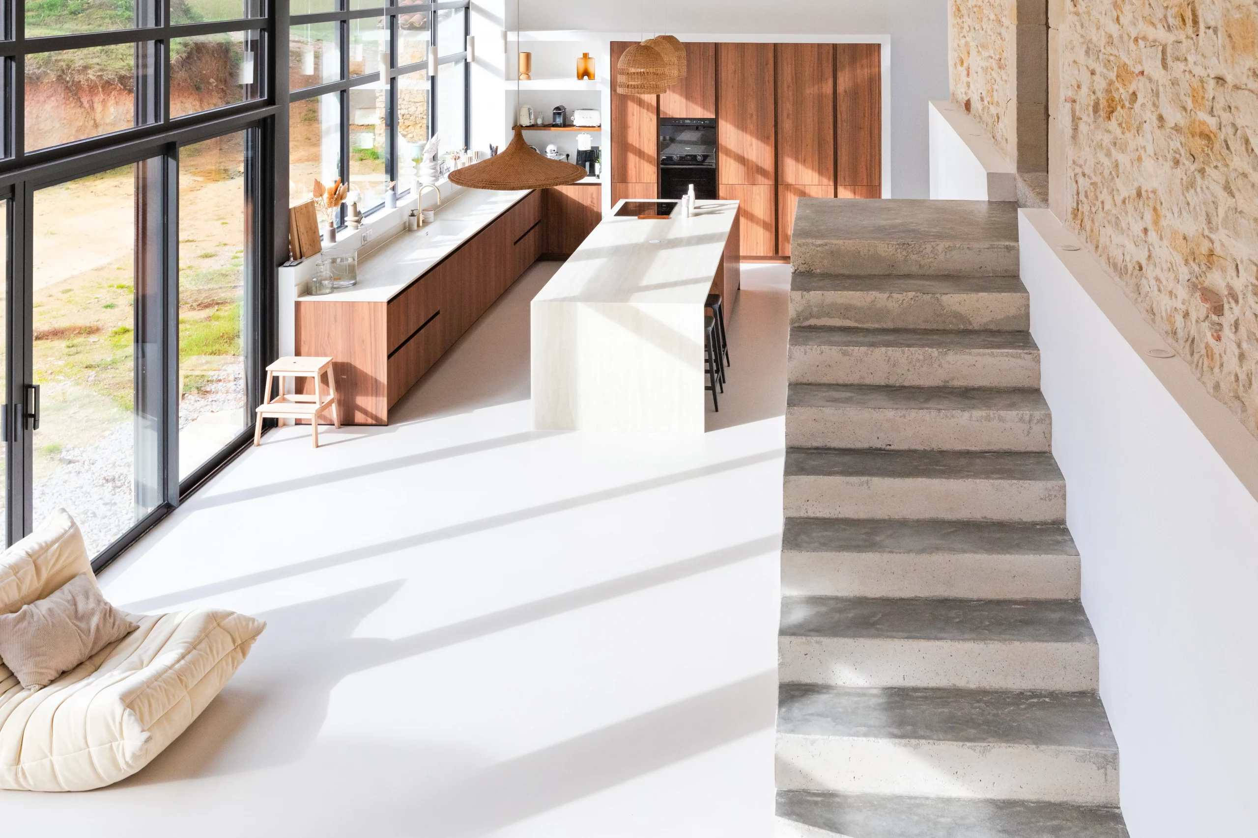 Cuisine avec îlot central, façades en décor bois, escalier clair et mur en pierre apparente
