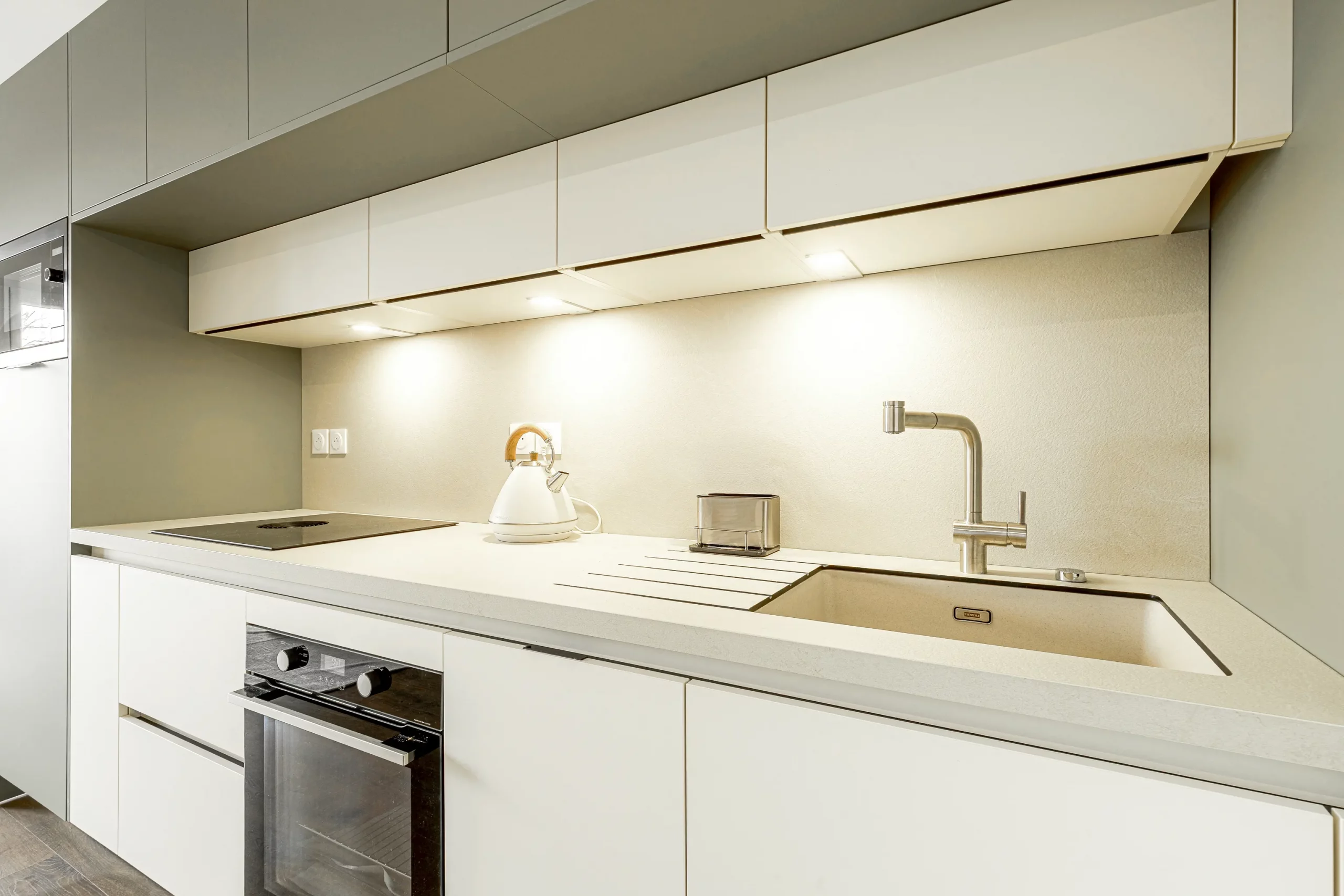 Détail d’une cuisine sur mesure avec évier, robinetterie inox, plan de travail clair et éclairage sous meubles hauts