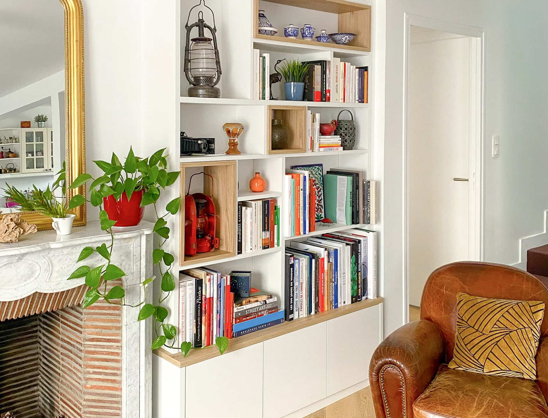 Détail d’une bibliothèque sur-mesure blanche et bois, avec niches ouvertes, livres, objets déco et rangements fermés en partie basse.