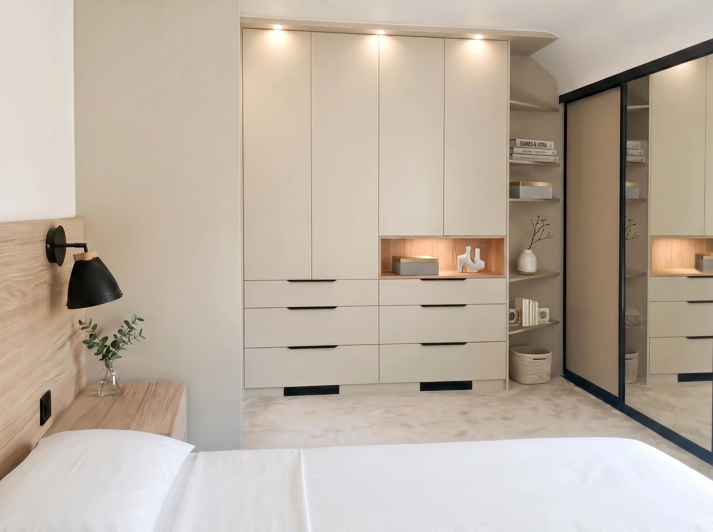 Dressing sur-mesure beige dans une chambre, avec portes toute hauteur, tiroirs bas, niche décorative en bois éclairée et portes miroir coulissantes.