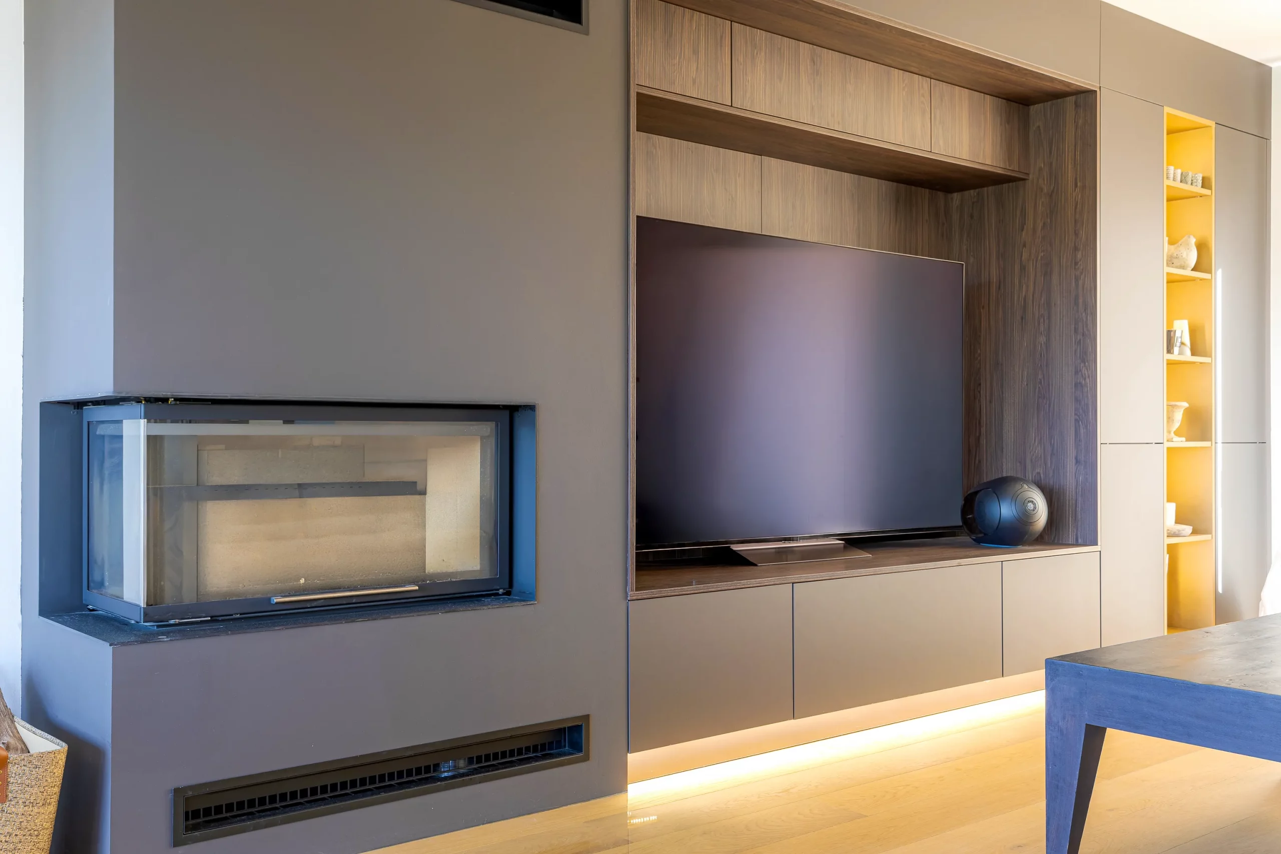 Aménagement TV sur mesure associant façades mates, décor bois foncé, éclairage indirect et cheminée intégrée au mur.
