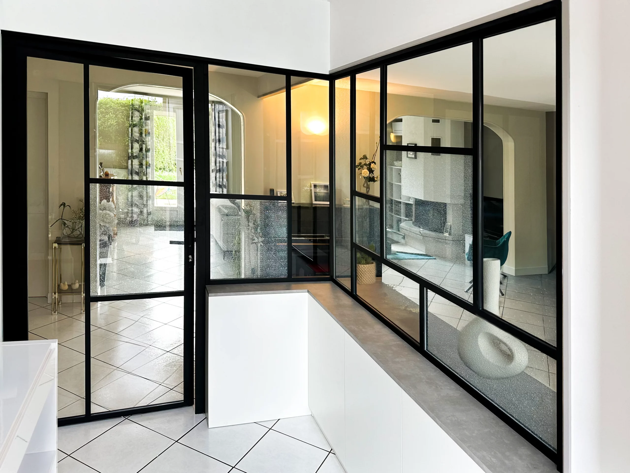 Verrière d’intérieur avec structure noire, rangements bas blancs et vitrage transparent pour créer une entrée sans fermer l’espace.