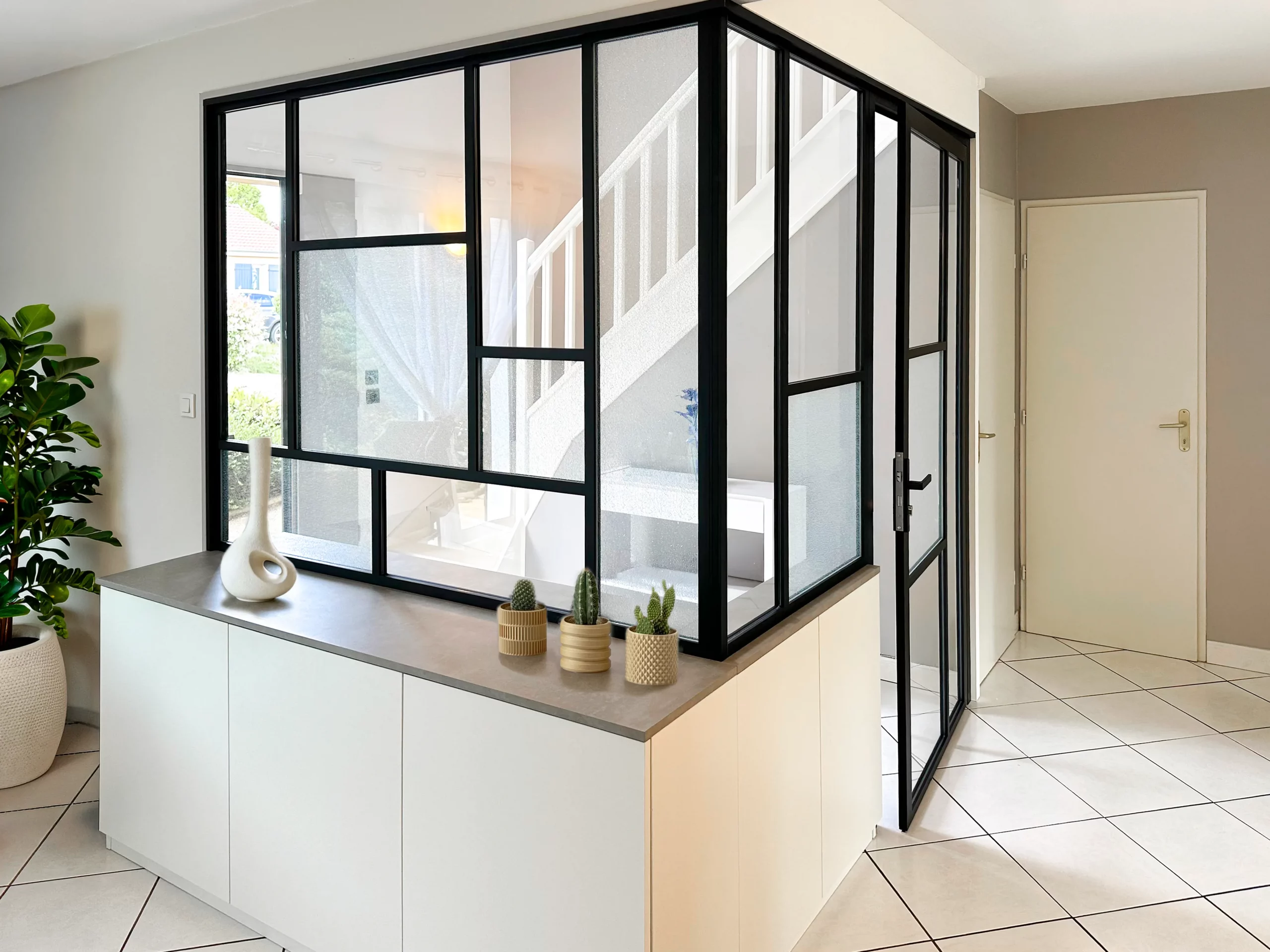 Verrière sur-mesure noire avec porte vitrée, soubassement blanc et plan de finition gris pour structurer l’entrée.