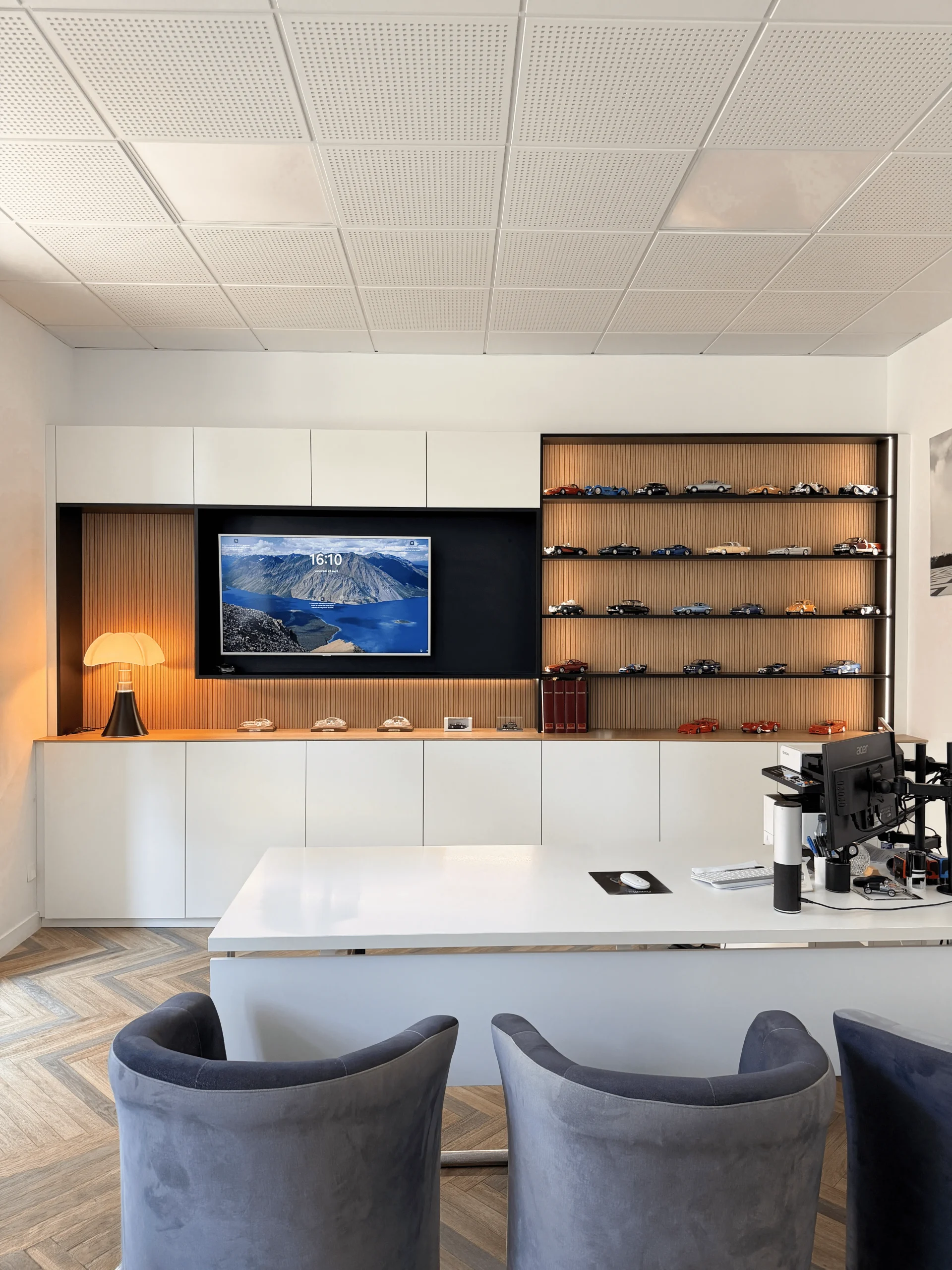 Aménagement mural sur-mesure pour bureau de notaire, avec meuble TV, rangements, étagères éclairées et présentation de petites voitures de collection.