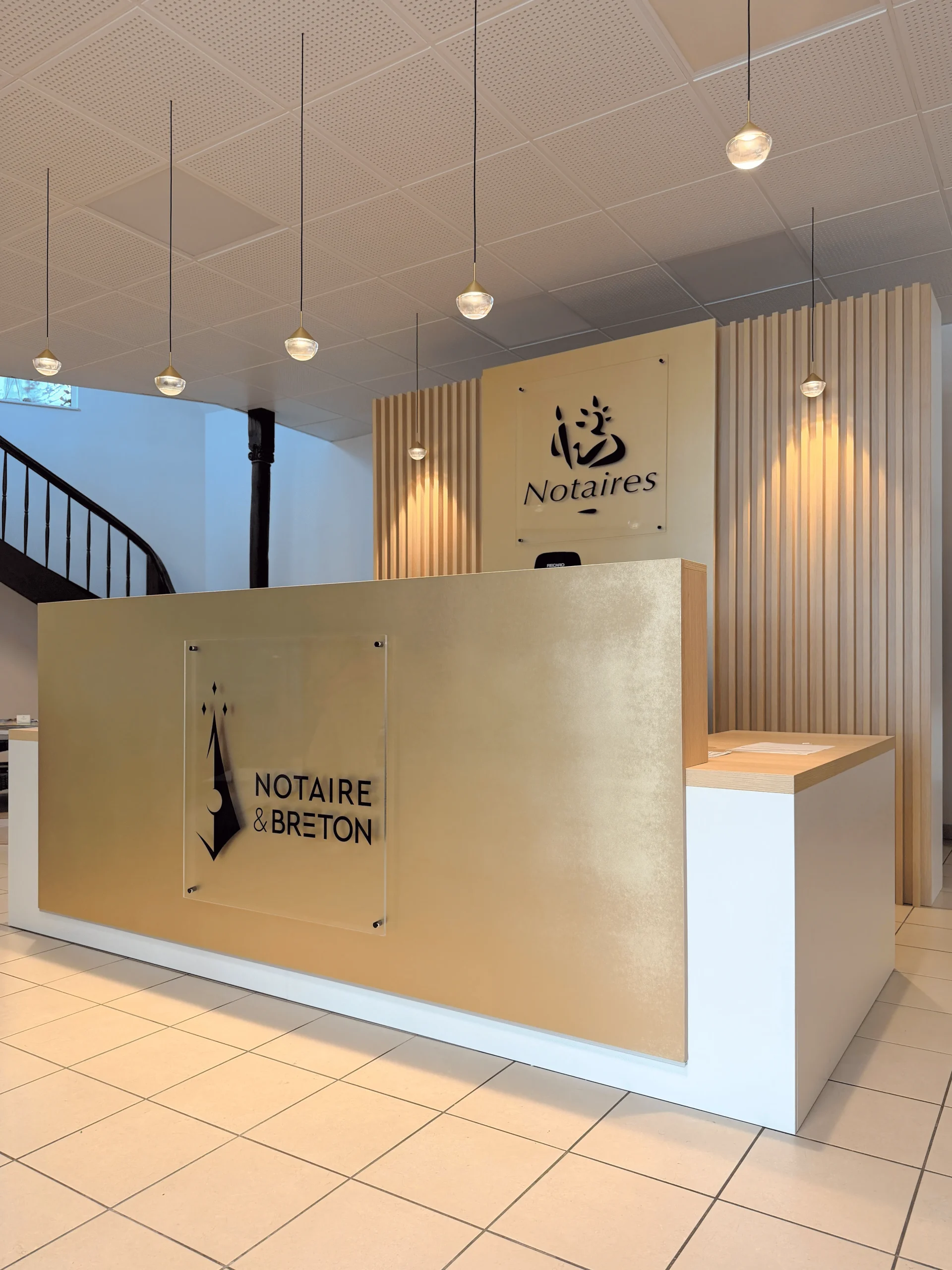 Banque d’accueil sur-mesure pour une étude notariale à Lannion, avec panneau décor effet laiton, enseigne intégrée et claustra bois.