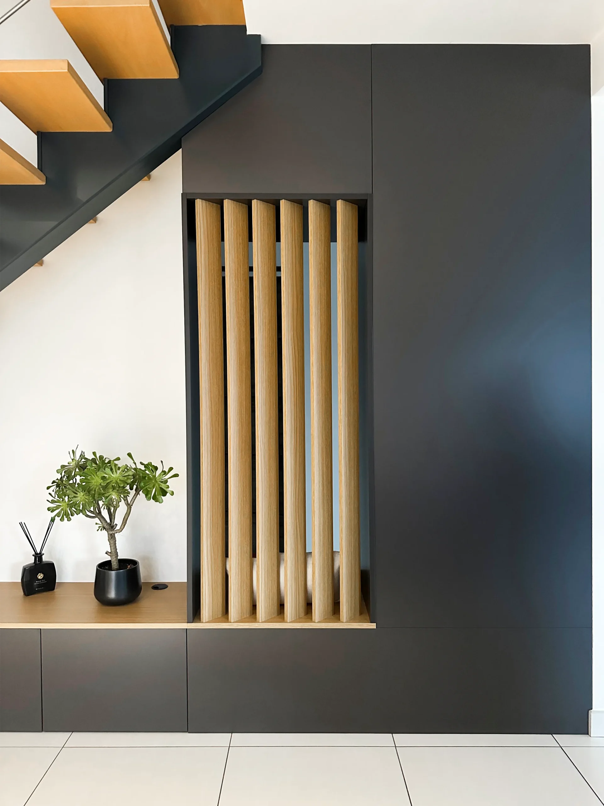 Claustra vertical en bois intégré à un meuble d’entrée sur-mesure avec rangements fermés et assise.