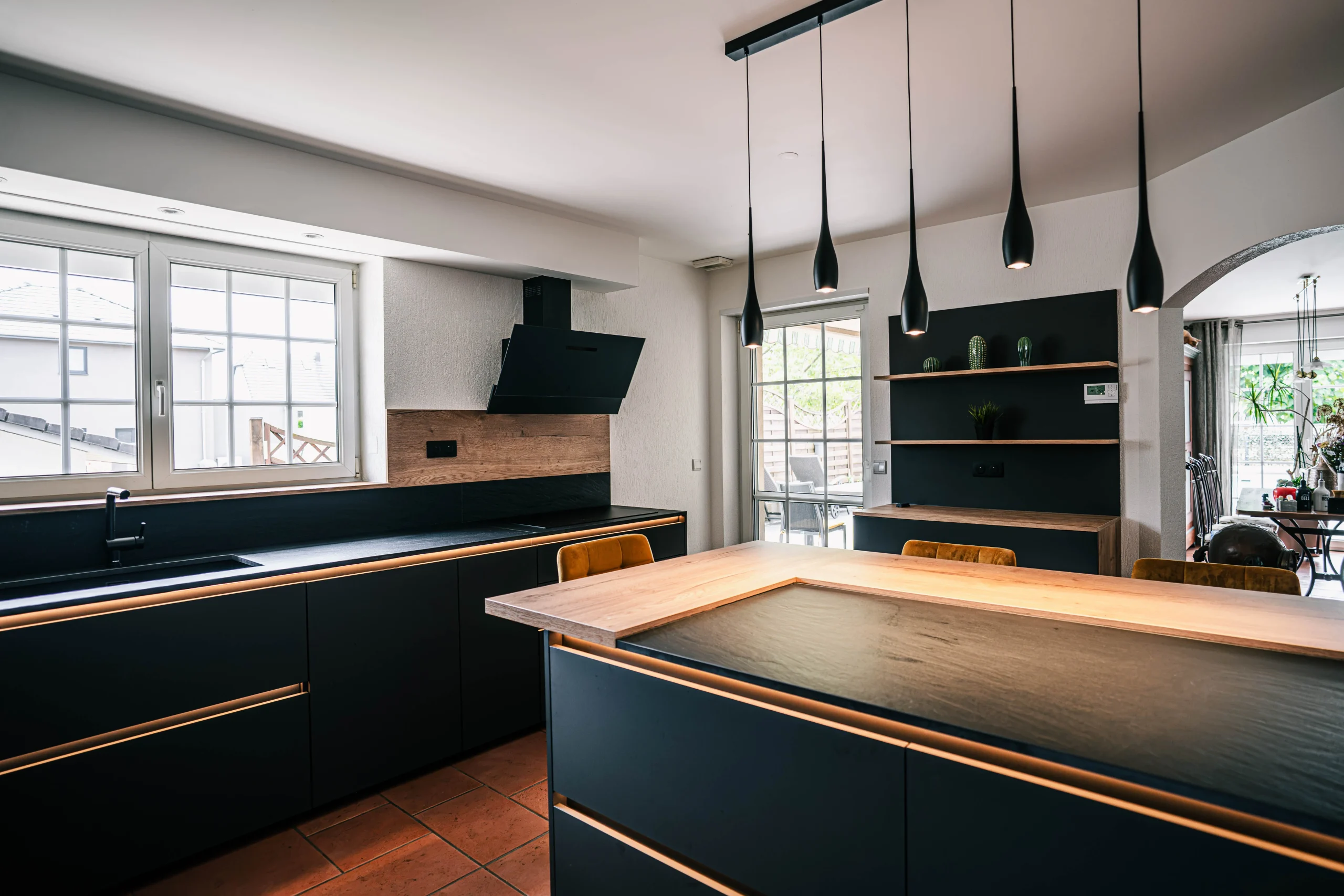 Vue de la cuisine sur-mesure réalisée à Kembs avec grand espace repas central, façades noires et touches de bois.