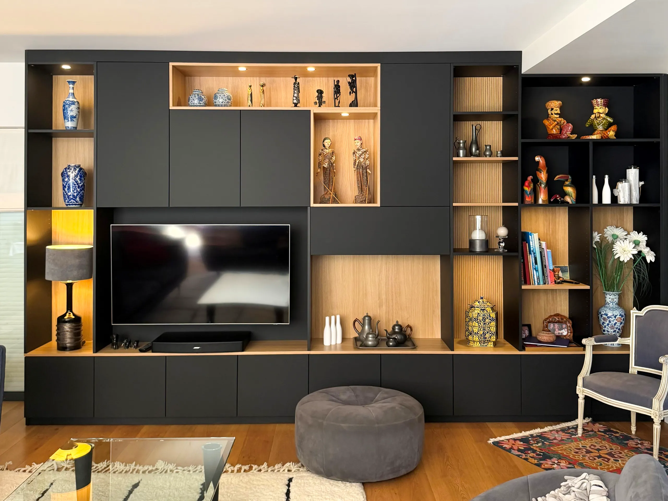 Composition murale sur-mesure en noir et bois avec meuble TV, niches décoratives, rangements bas et éclairage intégré.