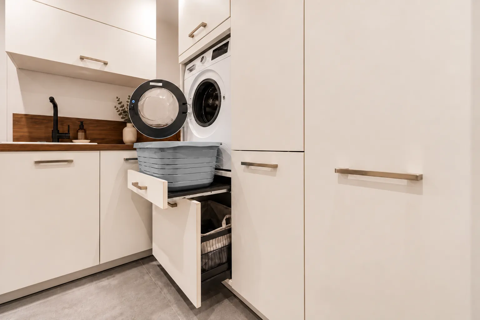Détail d’une buanderie sur-mesure avec lave-linge surélevé, tablette coulissante et rangements intégrés pour faciliter le tri et la gestion du linge.